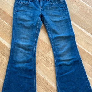 Blå bootcut jeans från Levis - Säljer ett par klassiska blå bootcut jeans från Levis med snygga detaljer på bakfickorna, bland annat en knapp och läderband. Jeansen har normal passform och är tillverkade i jeansmaterial. Perfekta för dig som gillar retrostil!