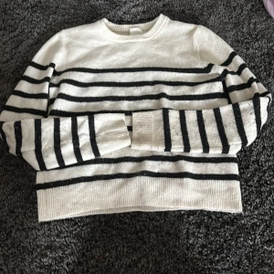 Vit och svart randig stickad tröja från H&M - Säljer en vit stickad tröja från H&M med svarta horisontella ränder. Tröjan har rund halsringning och långa ärmar. Perfekt för en stilren och avslappnad look.