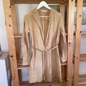 Beige byxdress från MSCH Copenhagen  - Snygg beige byxdress från MSCH med bälte i midjan och klassisk krage. Några små fläckar på ryggen