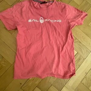 Rosa t-shirt från Sail Racing - Säljer en rosa t-shirt från Sail Racing med vit logga tryckt på bröstet och en mindre logga i nacken. Lite liten i storleken