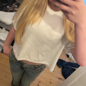 Vit croppad stickad tröja från H&M Divided - Säljer en vit croppad stickad tröja från H&M Divided. Tröjan har korta ärmar och rund halsringning. Perfekt för lager-på-lager och enkel att matcha med jeans eller kjol.