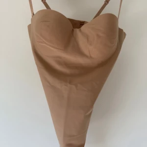 Skims body - Säljer en beige bodysuit med bygel och vadderade kupor. Den har justerbara axelband och en slät, figurnära passform. Perfekt att styla under kläder eller som topp till jeans eller kjol.