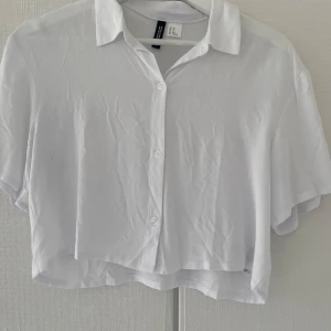 Vit croppad skjorta från H&M - Säljer en fräsch vit croppad skjorta från H&M. Skjortan har korta ärmar, klassisk krage och knäppning framtill. Perfekt till sommaren och enkel att styla med jeans eller kjol. Har aldrig använt💕