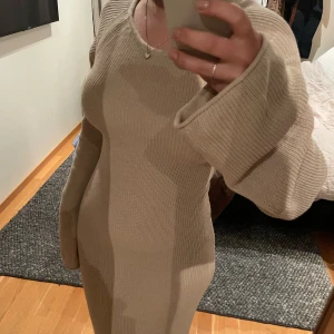 Beige stickad långklänning med snörning i ryggen - Säljer en beige stickad långklänning med lång ärm och rund halsringning. Klänningen har en tight passform och är perfekt för dig som gillar en enkel men stilren look. Supermjuk och skön att bära. Priset är förhandlingsbart vid snabb affär. 