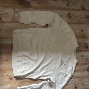 Beige sweatshirt från Axel Arigato - Säljer en stilren beige sweatshirt från Axel Arigato med broderad fågel på bröstet. Tröjan har rund halsringning och långa ärmar. Perfekt för en avslappnad och trendig look.