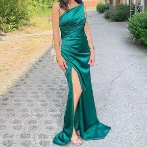 Grön långklänning i satin med slits  - Säljer en elegant grön långklänning i glansigt satinmaterial. Klänningen har en snygg design och en hög slits framtill som ger en extra touch. PRISET KAN DISKUTERAS