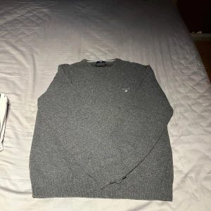 Grå stickad tröja från GANT - Säljer en klassisk grå stickad tröja från GANT i superfin lammull. Tröjan har rund halsringning, lång ärm och en liten broderad GANT-logga på bröstet. Perfekt för lager-på-lager och stilren vardagslook. Storlek L men passar även storlek M. Öppen för prisförslag!