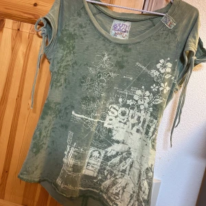 Grön t-shirt med blommigt tryck från South Beach Sport - Snygg grön t-shirt med blommigt och grafiskt tryck framtill från South Beach Sport. T-shirten har korta ärmar med knytband och rund halsringning. Perfekt för en avslappnad stil.