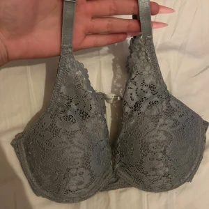 Grå spets-bh - Säljer en grå bh med vacker spetsdetalj och justerbara axelband. Bh:n har vadderade kupor och ger bra stöd. Perfekt för dig som vill ha något både snyggt och bekvämt. Säljs då den är för stor för mig 