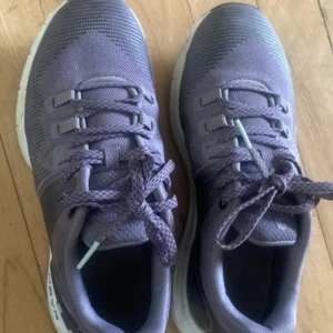 Lila sneakers från Under Armour - Säljer ett par lila/svarta sneakers från Under Armour med vit sula och snörning. Skorna har meshmaterial för bra andningsförmåga och en sportig look. Perfekta för träning eller vardagsstil.