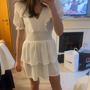 Vit volangklänning från Gina Tricot - Superfin vit kortklänning från Gina Tricot med v-ringning, volangdetaljer och smockad midja. Perfekt till skolavslutning eller andra sommartillfällen. Använd endast 2 gånger och har inga tecken på användning. Klänningen säljs inte längre💗