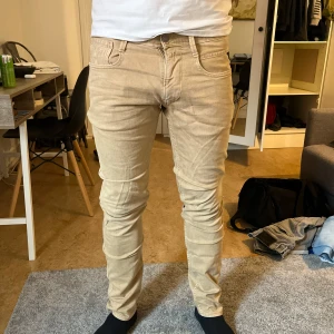 Beige Replay Anbass jeans - Säljer ett par snygga beige Replay Anbass jeans i klassisk femficksmodell. Byxorna har normal passform och raka ben, tillverkade i bomull med lite stretch för extra komfort. Perfekta för dig som vill ha stilrena och bekväma jeans.