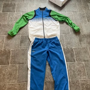 Lacoste tracksuit - Säljer ett par blå träningsbyxor från Lacoste Sport i samarbete med Daniil Medvedev. Byxorna har vita sidor, resår i midjan och klassisk Lacoste-logga på benet. Perfekta för sport eller chill. En liten skada på byxan som syns på bilden 