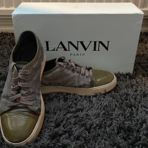 Grå sneakers från Lanvin med lackad tå - Säljer ett par grå sneakers från Lanvin med snörning och glansig, olivgrön lackad tå. Skorna har beige sula och ovandel i mocka. Klassisk och stilren design med exklusiv känsla.