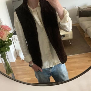 Brun manchesterväst från John Henric - Säljer en brun manchesterväst från John Henric med dragkedja framtill. Västen har diskreta ränder i tyget och är fodrad med polyester. Perfekt för lager-på-lager och ger en stilren look. Jag är 180 lång och passar fint! 