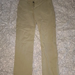 Beiga chinos från Hampton Republic 32/32 - Snygga beiga chinos från Hampton Republic med slim fit-passform och comfort stretch. Klassisk design med knapp och dragkedja framtill samt fickor både fram och bak. Perfekta för en stilren och avslappnad look.