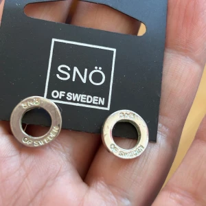 örhängen från SNÖ of Sweden - Säljer ett par stilrena, runda örhängen från SNÖ of Sweden. Örhängena har en cirkelformad design med märkets namn ingraverat runt kanten. Perfekta för dig som gillar minimalistiska smycken. Finns i Majorna,