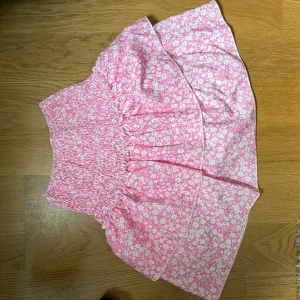 Rosa blommig kortkjol - Supersöt rosa kortkjol med vitt blommönster och smockad midja.