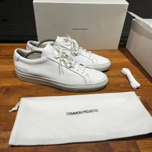 Common Projects Achilles Low White - Ett par skor från Common projects, Achilles Low White, som använts mindre än 10 gånger. Jag säljer på grund av de inte passar mig. Storlek 42 (lite stor i storlek), passar säkert 43. Bevis på att de är äkta finns och medföljer, om man vill ha mer bevis på att de är äkta skriv personligen. Skolåda, påse och skosnöre ingår.
