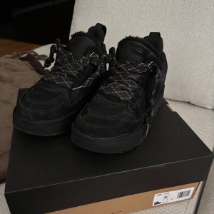 UGG Lowmel ”black” - Säljer ett par svarta UGG sneakers med grov sula och breda snören. Skorna har en chunky design och är tillverkade i syntetmaterial med mesh-detaljer. Perfekta för dig som gillar streetwear och vill ha något bekvämt och stilrent.