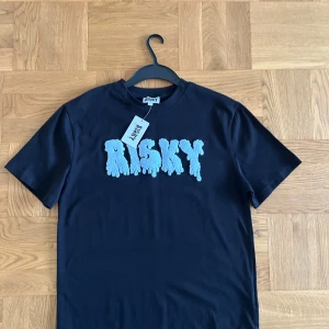 Svart t-shirt från Risky med blå text( HELT NY) - HELT ny svart tshirt från RISKY som har aldrig används tidigare och som har kvar prislappen.