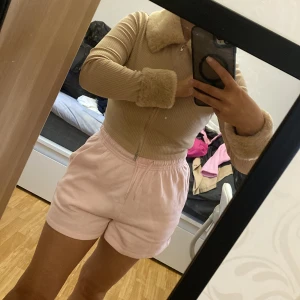 Beige ribbad kofta med fuskpälsdetaljer - Säljer en beige ribbad kofta med dragkedja framtill. Tröjan har mjuka fuskpälsdetaljer vid krage och ärmslut, vilket ger en mysig och trendig look. Perfekt för dig som vill ha något både snyggt och bekvämt.