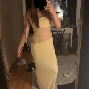 Ljusgul långklänning med spetsdetaljer - Säljer en ljusgul långklänning med smala axelband och transparent spets över magen. Klänningen har figurnära passform och är perfekt för sommarens tillfällen. Materialet känns mjukt och följsamt.