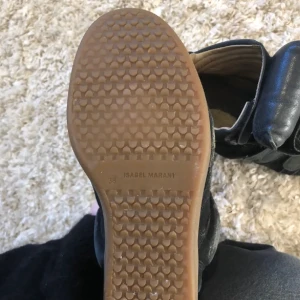 Svarta sneakers med kilklack från Isabel Marant - Säljer ett par svarta Isabel Marant sneakers med kilklack och kardborreband. Skorna har platt gummisula och är tillverkade i mocka och skinn. Kommer med originalkartong. Perfekta för dig som vill ha en trendig look. Något slitna på lädret upptil, se sista bilden 