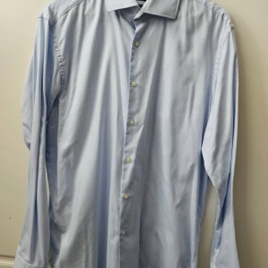 Hugo Boss blå skjorta, storlek 44 - Ljusblå skjorta från Hugo Boss i modellen Regular Fit. Skjortan har långa ärmar och knappar framtill. Nypris 1199 kr. Se sista bild där det har gulnat på kragen. Annars I fint skick
