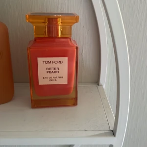 Tom Ford Bitter Peach Eau de Parfum 100 ml - Exklusiv parfym från Tom Ford i doften Bitter Peach. Flaskan är fyrkantig och har en intensiv orange färg med en transparent orange kork. Innehåller 100 ml Eau de Parfum. Perfekt för dig som gillar fruktiga och lyxiga dofter.