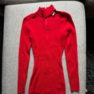 Röd ribbad långärmad klänning med hög krage - Säljer en tight röd klänning med lång ärm och hög krage. Klänningen har en unik asymmetrisk cut-out vid halsen och är ribbad i materialet. Perfekt för dig som vill sticka ut med en trendig look.