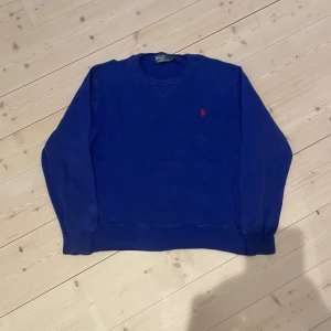Blå tröja från Polo Ralph Lauren - Klassisk blå tröja från Polo Ralph Lauren med röd broderad logga på bröstet. Tröjan har rund halsringning och långa ärmar, perfekt för en stilren look. Storlek large men skulle säga att den passar M. Skick 10/10, det är bara att skicka om ni undrar något!