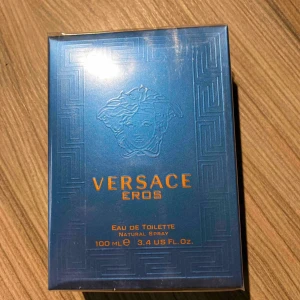 Versace Eros Eau de Toilette 100 ml - Versace Eros Eau de Toilette för herr, 100 ml. Flaskan är blå med guldiga detaljer och har ett klassiskt Medusa-huvud på framsidan. Parfymen kommer i en lyxig blå kartong med guldtext och grekiskt mönster. En ikonisk doft från Versace.