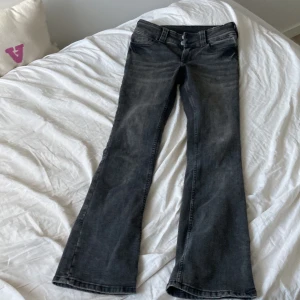 Grå bootcut jeans från H&M - Säljer ett par grå bootcut jeans från H&M med justerbar midja. Jeansen har dubbla knappar och dragkedja framtill samt fickor med lock bak. Perfekta för dig som gillar en klassisk jeanslook med  utsvängda ben.