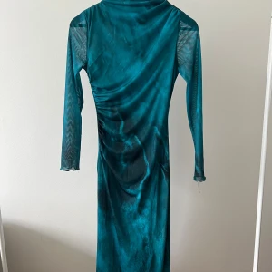 Turkos långklänning i mesh - Säljer en turkos långklänning i mesh med långa ärmar och lätt rynkade detaljer på sidan. Klänningen har en smal passform och är tillverkad i ett tunt, stretchigt material som ger en cool look.