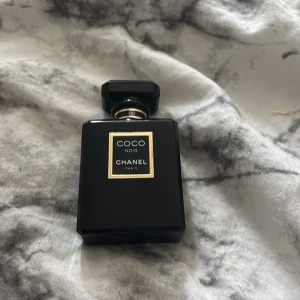 Coco Noir Eau de Parfum från Chanel 50 ml - Elegant parfymflaska i svart glas med guldiga detaljer från Chanel. Doften är Coco Noir Eau de Parfum och flaskan rymmer 50 ml. Flaskan har en klassisk, lyxig design med fyrkantig form och svart lock. Uppskattningsvis cirka 35/50 ml kvar, pris kan diskuteras.