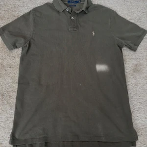 Mörk grön pikétröja från Polo Ralph Lauren - Säljer en klassisk mörk grön pikétröja från Polo Ralph Lauren med broderad logga på bröstet. Tröjan har korta ärmar, krage och knappar framtill. Modellen är custom slim fit och passar perfekt till en avslappnad stil.