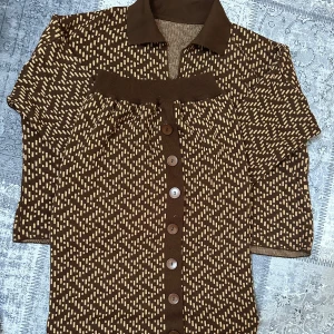 Brunmönstrad kofta med krage - Säljer en brun kofta med beige mönster och stora knappar framtill. Koftan har klassisk krage och långa ärmar. Materialet känns stickat och mjukt, perfekt för lager-på-lager. Passar dig som gillar retrostil.