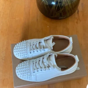 Vita loubs  - Säljer ett par vita sneakers från Christian Louboutin med coola vita nitar på tån och den ikoniska röda sulan. Skorna har snörning och är tillverkade i skinn, vilket ger en lyxig känsla och edgy look. Köpte de på Plick och vet att de är äkta då jag har en bild på kvittot för 2800kr så där av priset ❣️