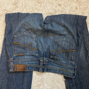 Mustang jeans  - Säljer ett par klassiska blå jeans från Mustang med snygga kontrastsömmar och broderade bakfickor. Byxorna har normal passform och raka ben, samt läderpatch med logga bak. 