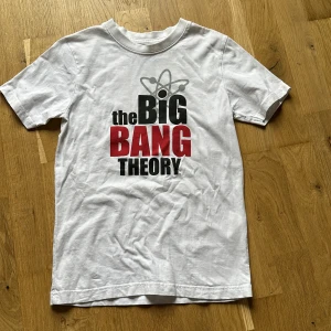 Vit t-shirt med The Big Bang Theory-tryck - Vit t-shirt med tryck med  The Big Bang Theory på bröstet. Klassisk passform och rund halsringning. Perfekt för fans av serien som vill ha en enkel och snygg t-shirt med ikoniskt motiv.