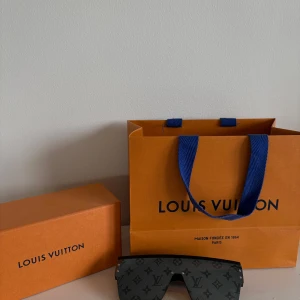Svarta solglasögon från Louis Vuitton - Snygga svarta solglasögon från Louis Vuitton med monogrammönster på glaset och breda skalmar med logotyp. Glasögonen har en modern, oversized sköldform och är tillverkade i Italien.