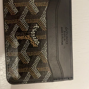 Go7ard brun mönstrad plånbok - Säljer en exklusiv plånbok från Go7ard i brunt och svart med deras ikoniska grafiska mönster. Plånboken har flera kortfack och är tillverkad i skinn med detaljer i beige och vitt. Kommer i original grön ask med silverlogga.