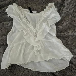 Vit volangblus med v-ringning - Supersöt vit blus med v-ringning och volangdetaljer längs halsen och axlarna🤍storlek m men passar även mig som bär xs/s