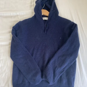 Mörkblå hoodie i merinoull från Say Less - Mysig mörkblå hoodie från Say Less i merinoull. Tröjan har huva med snörning och långa ärmar, perfekt för kyliga dagar. Enkel och stilren design som passar till många olika outfits.