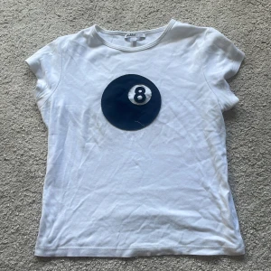 Vit t-shirt med 8-ball från Subdued M - Vit t-shirt från Subdued med ett stort svart 8-ball tryck på bröstet. Klassisk rund hals och korta ärmar. Skön och mjuk i bomull, perfekt till jeans eller kjol för en chill vibe.🎱🤍🪽