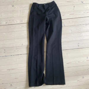 Svarta bootcut kostymbyxor BikBok - Svarta kostymbyxor från BikBok i storlek 34. Byxorna har bootcut-modell med pressveck och diskreta bakfickor. Snygg passform och klassisk look, perfekta till en trendig outfit.