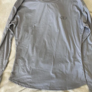 Ljusgrå långärmad tröja från OTP - En stilren ljusgrå långärmad tröja från OTP i mjukt och stretchigt material. Tröjan har en enkel design med rund halsringning och diskret logga på bröstet. Perfekt för en clean och avslappnad look.