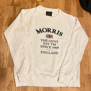 Vit sweatshirt från Morris - Medium - Vit sweatshirt från Morris i 100% bomull i storlek Medium med broderad Union Jack och text på bröstet. Klassisk rund hals, ribbade muddar och relaxed fit. Perfekt för dig som gillar brittisk preppy stil och vill ha något stilrent men ändå casual.