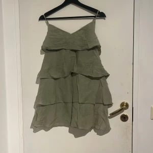 Klänning - Supersöt ljusgrön kortklänning med flera lager volanger och tunna axelband. Klänningen har v-ringad hals och är tillverkad i ett lätt, flowy material som ger en luftig känsla. Perfekt för varma dagar när du vill känna dig extra fin.